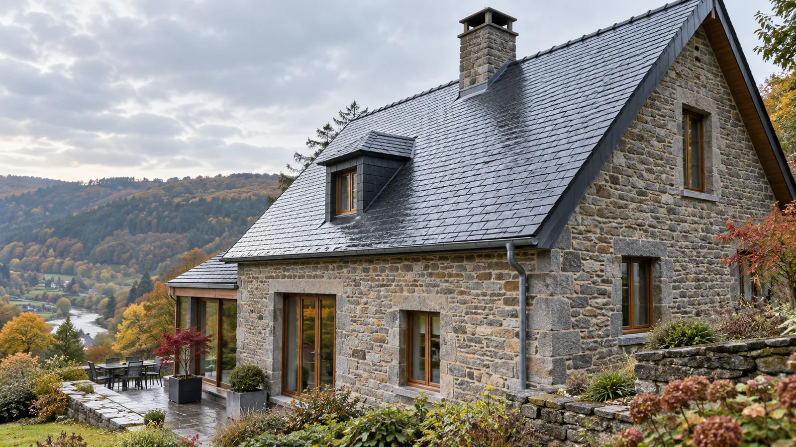 Maison en pierre des Ardennes couverte d'ardoises naturelles gris-bleu, avec une vallée boisée en automne à l'arrière-plan